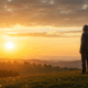 An emotional, photorealistic, wide-angle shot. A healthy and revitalized 76-year-old man stands on a gentle hill, facing a magnificent, warm sunrise. His posture is relaxed but strong, taking a deep, peaceful breath. The image is filled with the golden light of dawn, symbolizing a new beginning, hope, and freedom from fear.