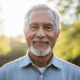 Conclusion (Empowered Senior): Uplifting portrait of the same 78-year-old man from the intro, now standing outdoors, looking directly at the camera with a confident, healthy, and reassuring smile. Bright, natural sunlight, background slightly blurred. The image conveys hope, wisdom, and control over his health.