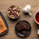 Prompt: A vibrant and artful flat lay composition showcasing the five guardian foods. A piece of baked salmon, a small bowl of mixed beans, a few squares of dark chocolate, a steaming cup of tea, and a head of garlic are beautifully arranged on a rustic wooden surface. The arrangement is harmonious, like a symphony of colors and textures. Style: Bright, uplifting light, top-down view, highly detailed, photorealistic, 8K.